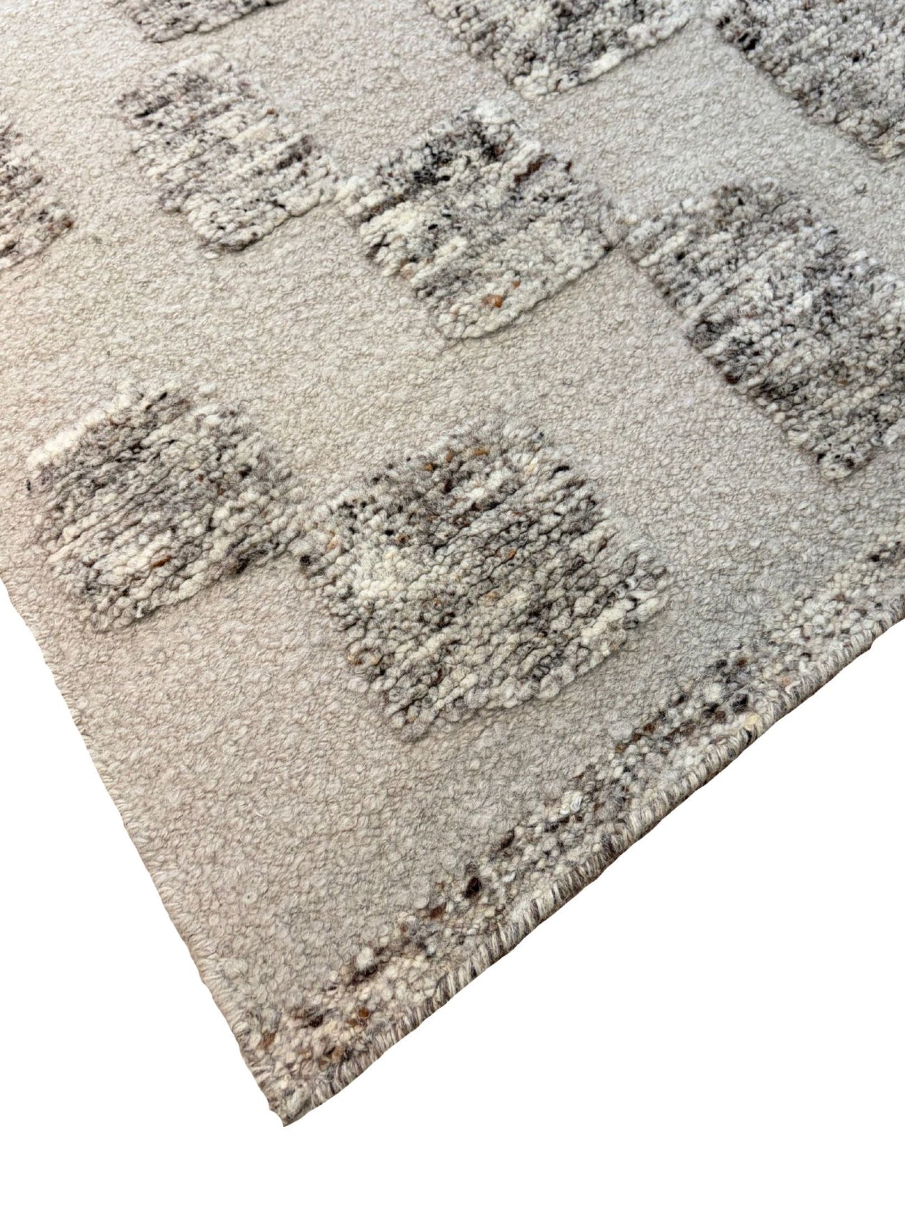 A close-up of a textured area rug with a geometric pattern of raised, chunky squares in gray, beige, and off-white on a light cream background.