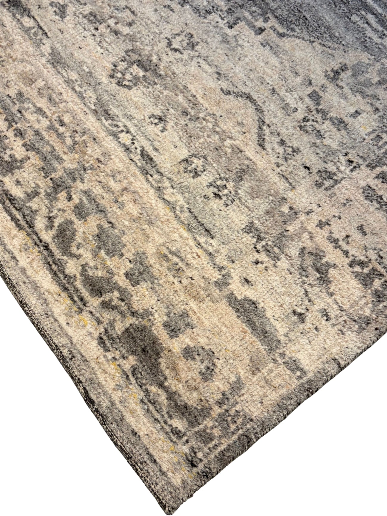 A close-up of a distressed area rug showing its corner, featuring a mottled pattern in beige, gray, and charcoal tones.