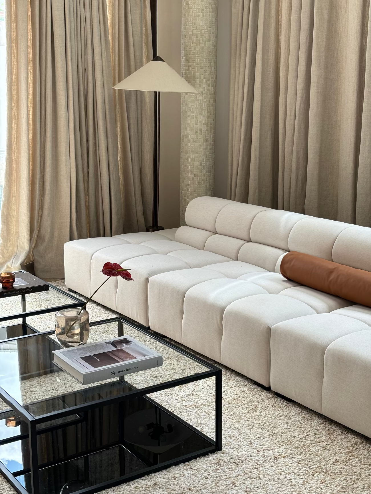 Modern living room with a beige sectional sofa, glass coffee table, and curtains.